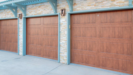 Panorama Garage exterior with wall-mounted light blue pergola and doorframe. There are three wooden sectional doors and stone veneer wall sidings.の写真素材