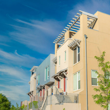 Square Whispy white clouds Fenced residential buildings with stairs to the verandas at Daybreak in South Jordan, Utah. There is a concrete sidewalk at the front of the buildings on the left and lawn on the right.の写真素材