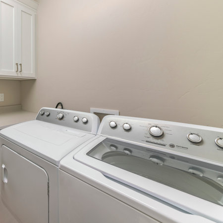 Square Interior of a laundry room with top cabinets and countertop. There are two laundry units on the right side near the counter below the wall cabinets with white wooden doors.の写真素材