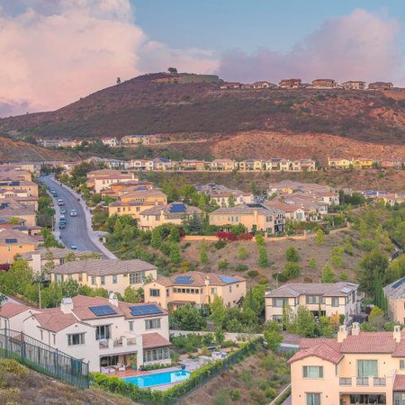 Square Puffy clouds at sunset Residential area in between the mountains against the colorful sky at San Diego, California. There are large houses and cars on the road at the left side against the mountain with houses on top.の写真素材
