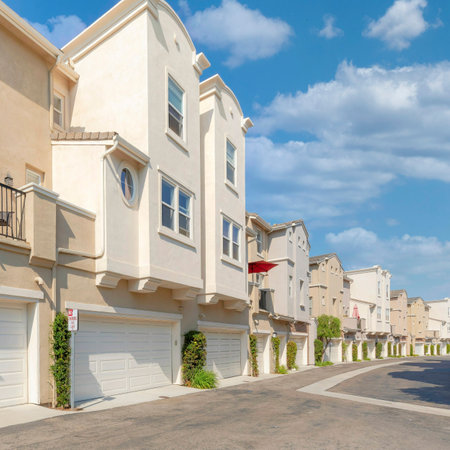 Square White puffy clouds Cream colored townhouses with attached garage asphalt driveway. Townhomes building with balconies and shrubs outside the white garage sectional doors at San Marcos, California.の写真素材