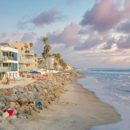 Square Puffy clouds at sunset Beach area at Oceanside in California with clothes on the natural rock seawall. There are buildings on the left with different designs and balconies with a view of the waterfront on the right.の写真素材