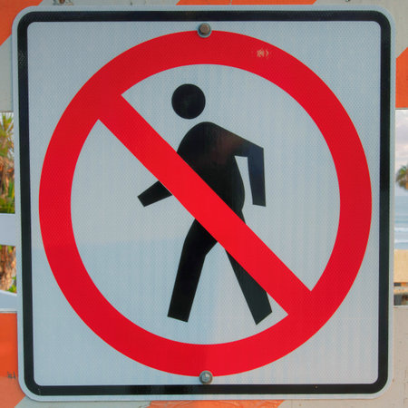 Square Puffy clouds at sunset No jaywalking sign on a white and orange barricade at Oceanside, California. Signage with a view of the beach waves, trees and fence at the back.の写真素材