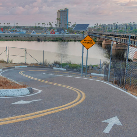 Square Puffy clouds at sunset Two-way curved downhill bike path at Oceanside, California. Bike trail near the river with Watch for Maintenance sign and solar panel on a post and a city view at the background.の写真素材