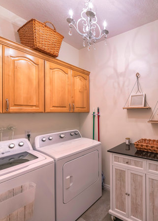 Vertical Craftsman laundry room with cabinets and hanging shelves. There are laundry machines on the right below the wall cabinets with woven basket on top across the wood planks wall with wreath on right.の写真素材