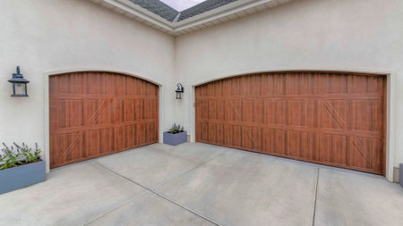 Panorama Puffy clouds at sunset Decorated three-car garage exterior with wall lamps and two wooden doors. Double garage doors with flowers on a gray wooden box on each side of the doors.の写真素材