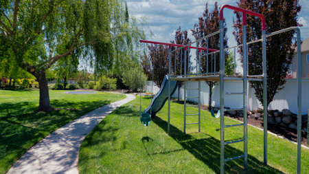Panorama White puffy clouds Outdoor park with trees in a residential community area at Utah. There is playground near the vinyl fence on the left against the view of a residential building and a concrete walk way on the right.の写真素材
