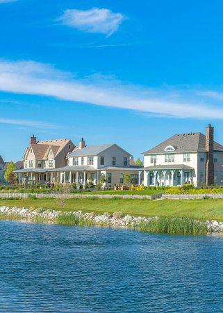 Vertical Whispy white clouds Blue water of Oquirrh Lake with rocks and grass on the shoreline. Lake in the middle of large residential houses at Daybreak, Utah.の写真素材