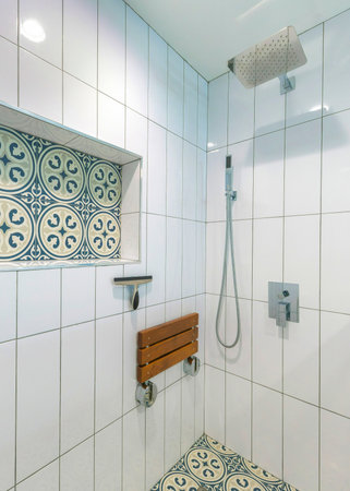 Vertical Shower stall interior with white ceramic tiles surround and cement tiles with blue patterns. There are wall mounted and handheld shower heads near the adjustable soap dish on the right.の写真素材