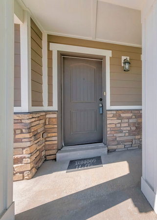 Vertical Porch of a house with white column posts and red arm chair. Exterior of a house with stone veneer siding and brown front door with lockbox.の写真素材