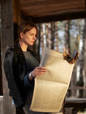 A young woman stands on the porch and reads hot news. A young woman stands on the porch and reads a burning newspaper.の写真素材