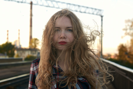 Blonde in a plaid shirt in windy weather on railway tracks. A blonde girl in a plaid shirt walks...