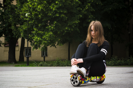 The girl on the street sits on a hoverboard.