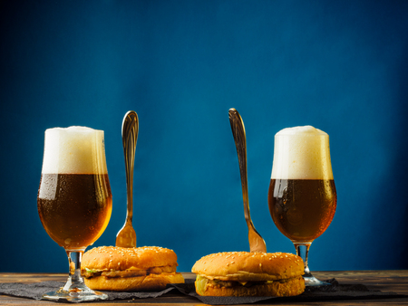 Two traditional hamburgers on a wooden table and with glasses full of foamy light beer.の写真素材