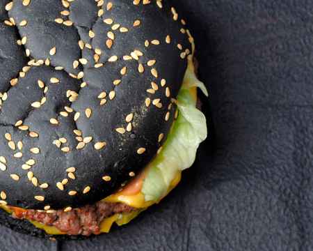 Black hamburger on a blue background. Black hamburger, Beef cutlet, pickled gherkins, lettuce leaves, Cheddar double cheese and jalapeno peppers.の写真素材