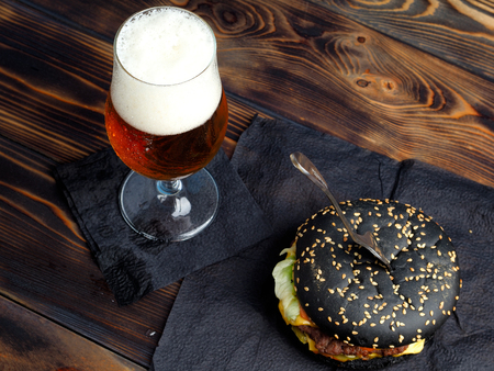 Set of beer and hamburger on a wooden table top view. Black hamburger and light beer.の写真素材