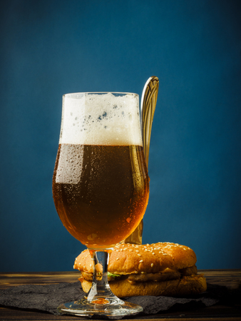 A traditional hamburger on a wooden table with a stack full of foamy light beer.の写真素材