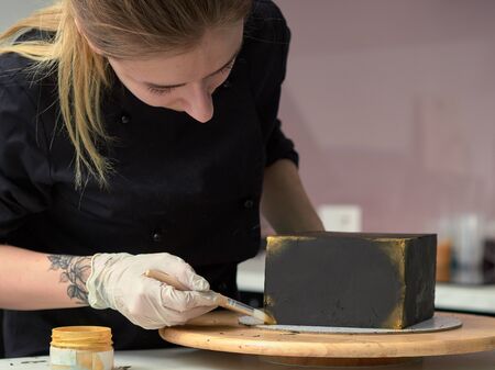 Step-by-step preparation of black designer cake. The confectioner decorates a black cake, gold food paint.の写真素材