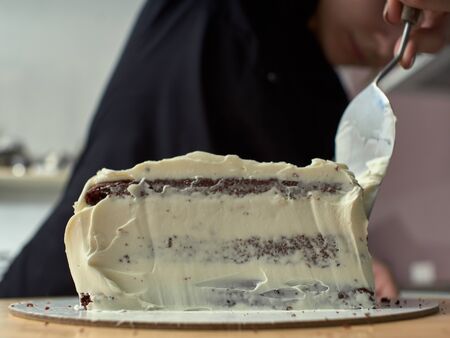 Step-by-step preparation of black designer cake. The confectioner covers the cake with cream.