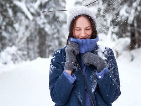 brunette walks through the winter forest in a gray hat, blue sweater and blue coat.