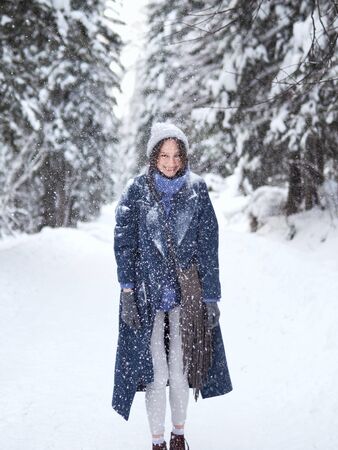brunette walks through the winter forest in a gray hat, blue sweater and blue coat.の写真素材