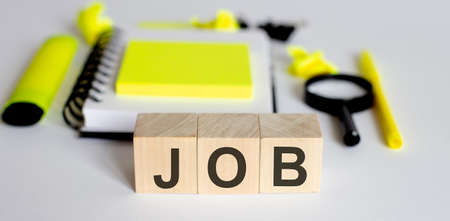 Text JOB on wooden cubes on a white background with office tools. Business