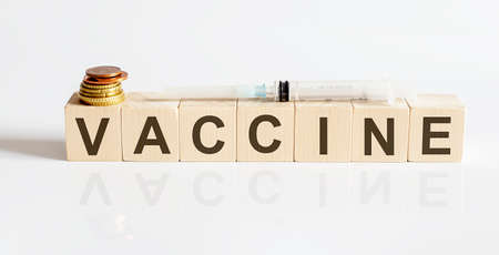 Vaccine inscription on wooden blocks under syringe with coins on white backgrond. Medicineの写真素材