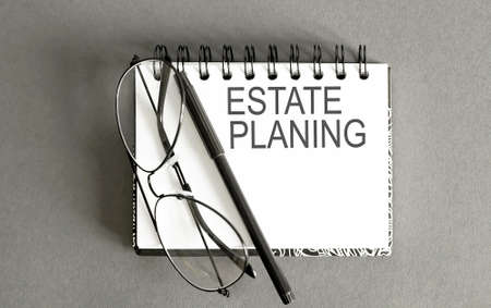 Business concept - Top view notebook writing ESTATE PLANNING on gray background with pen and glassesの写真素材