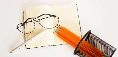 Pencil laying on an opened note pad isolated on white background with glassesの写真素材