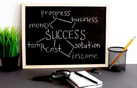 Success strategy concept hand drawn on black blackboard with notebook end office tools