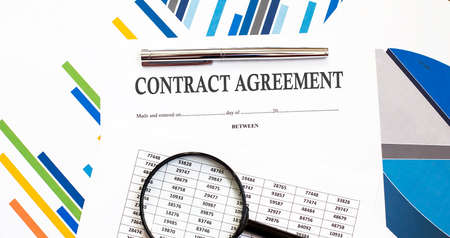 CONTRACT AGREEMENT on charts background with pen and magnifierの写真素材