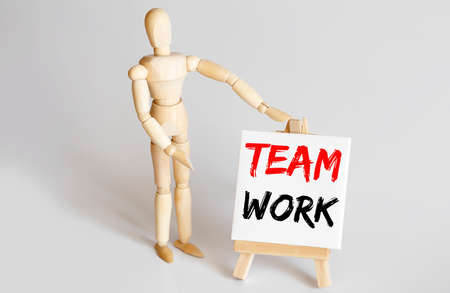 Wooden man shows with a hand to white easel with text TEAM WORK on white backgroundの写真素材