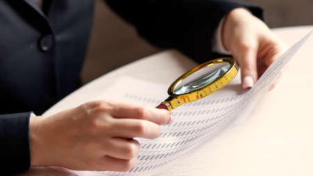 Close up of a woman looking at chart with a magnifying glass in her officeの写真素材