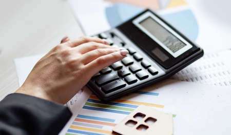 Woman calculating receipts lying on the chart with wooden house