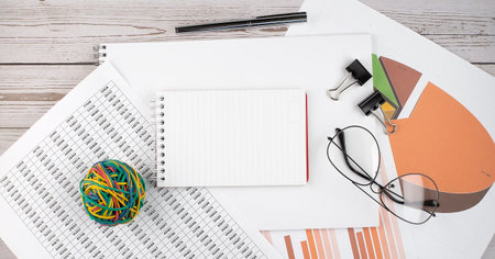 An empty Notepad with a pen, office tools and graphs on the desktop. Copy space