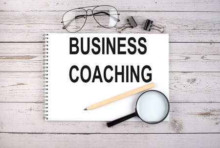 Notebook with text BUSINESS COACHING on wooden table with pen, magnifier and glassesの写真素材