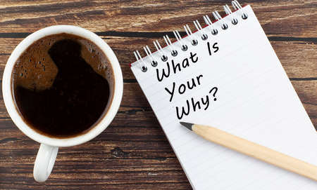 WHAT'S YOUR WHY text on the notebook with coffee on wooden background