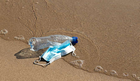 A plastic bottle lies and medical mask on the beach and pollutes the sea. The concept of pollution control the seas and oceans by plastic.の写真素材