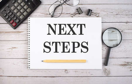 Blank notebook with text NEXT STEPS on the white background with calculator and office tools.の写真素材