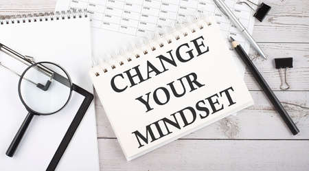 Notepad with text CHANGE YOUR MINDSET with a pen, office tools and graphs on desktop.