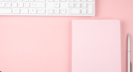 Pink office desk with keyboard and notebook. Top view, copy spaceの写真素材