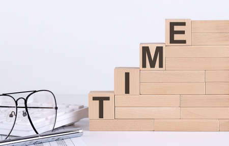 wooden cubes with letters TIME on white table with keyboard and glassesの写真素材