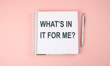 WHAT'S IN IT FOR ME text on notebook with pen on pink backgroundの写真素材