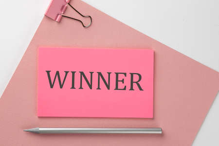 Pink sticker on pink paper with pencil on white background with text WINNERの写真素材