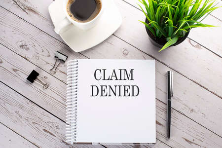 Cofee cup, notepad, pen on the wooden background. Business concept. Text CLAIM DENIEDの写真素材