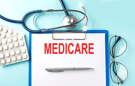 Paper with text MEDICARE on blue background with stethoscope and pillsの写真素材