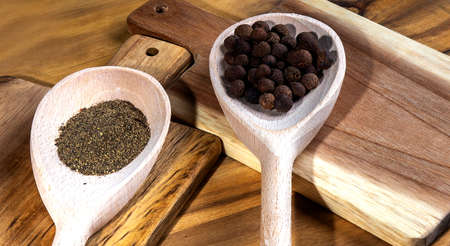 Black papper in spoon on wooden cutting board