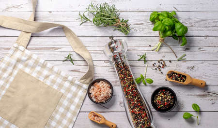 Kitchen beige apron, wooden spoon with spices, pepper mill, wood kitchen utensils on wooden background. top view.の写真素材