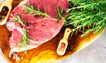 Raw beef steak with rosemary and spices on the wooden boardの写真素材