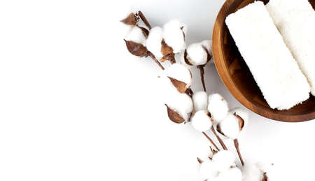 White cotton towels in wooden bowl and cotton plant flower branch on a white background. copy space